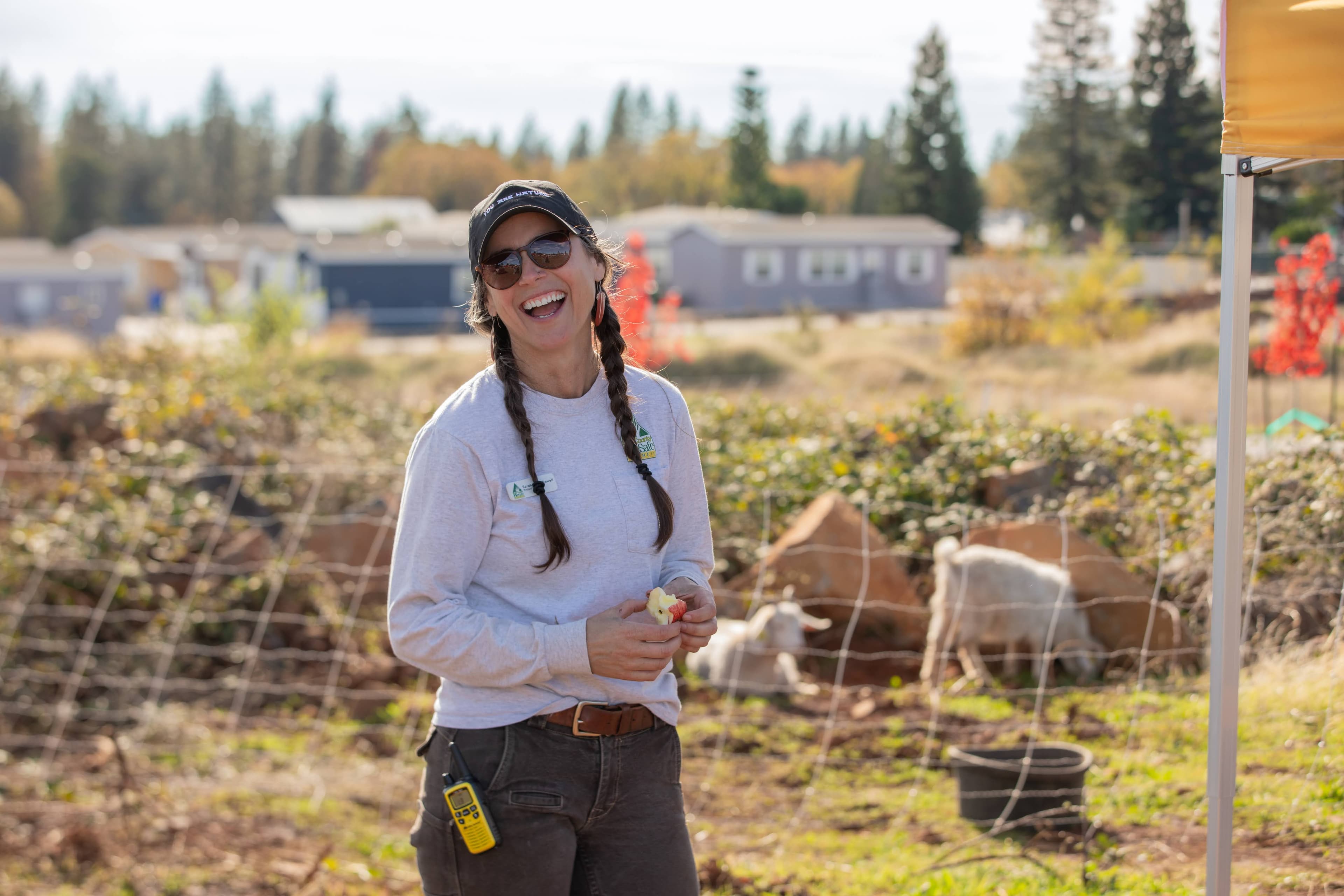 BCFSC staff member smiling at a community grazing event with goats grazing in the background